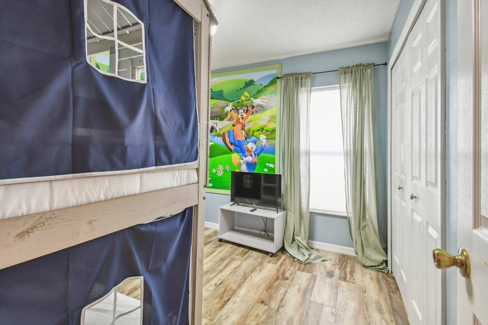 Welcome to a bright and cheerful room with a fun bunk bed and a colorful mural. Enjoy the natural light pouring in, highlighting the stylish laminate flooring and cozy TV setup, ideal for your relaxation.