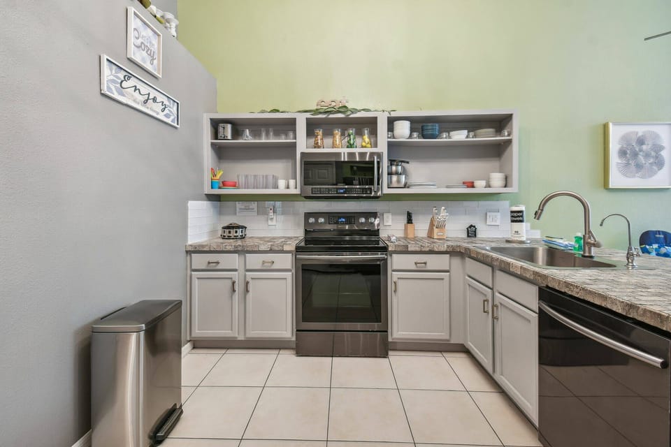 Enjoy a modern kitchen featuring stainless steel appliances, granite countertops, and light gray cabinets for ample storage. The soft green wall adds a refreshing touch, creating an inviting atmosphere for your meal preparation.