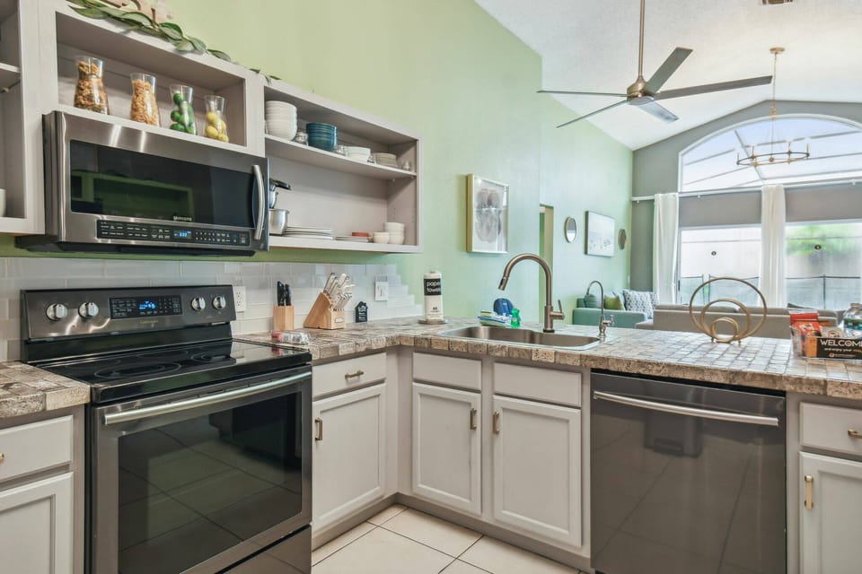 This inviting kitchen inspires culinary creativity with modern stainless steel appliances and a charming light green accent wall, open shelving for decorative items, and plenty of natural light for a warm, welcoming atmosphere.