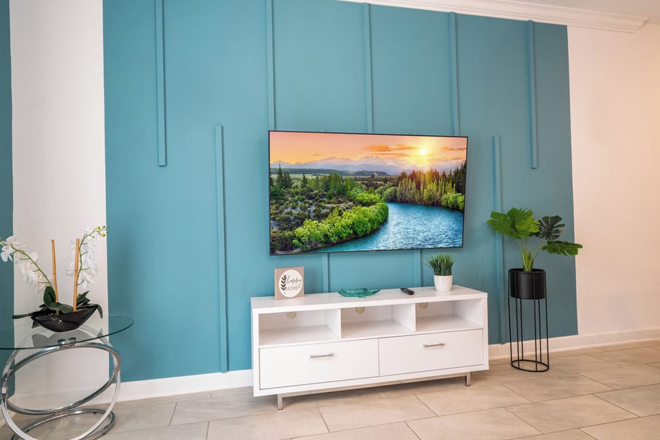Feature wall focus: large smart TV on striking teal paneling with a modern console and greenery-fresh, contemporary vibes.