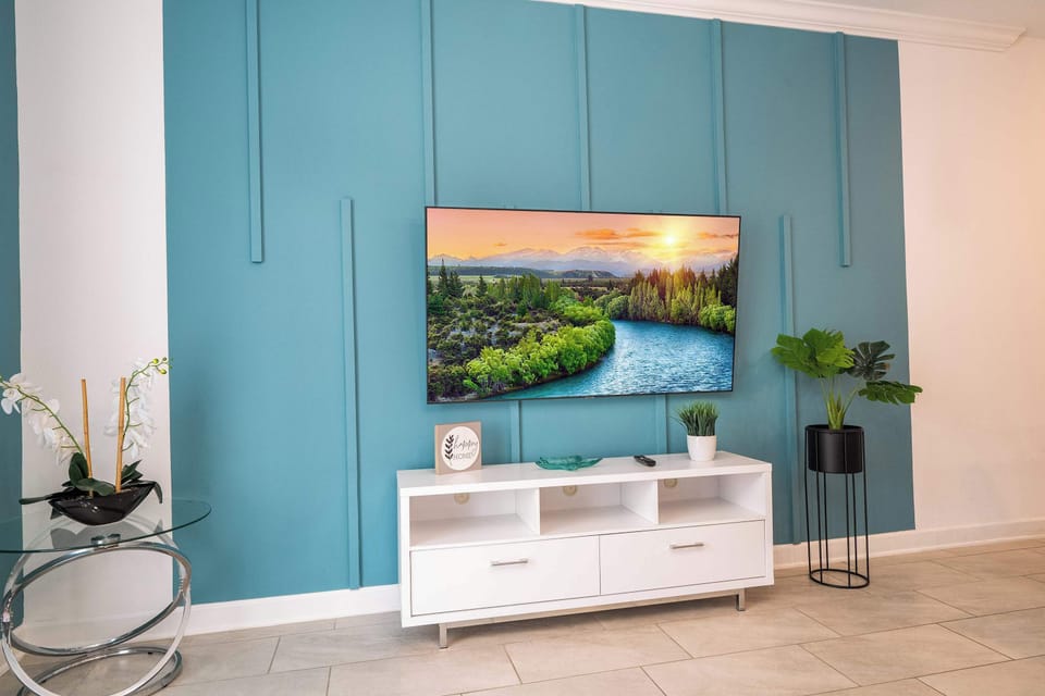 Feature wall focus: large smart TV on striking teal paneling with a modern console and greenery-fresh, contemporary vibes.