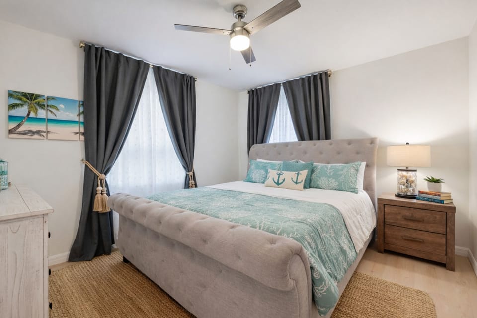 Serene coastal bedroom with king bed, blackout drapes, and ceiling fan