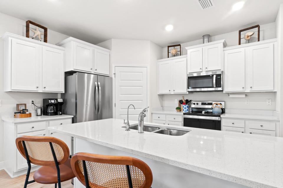 Your bright, fully-equipped kitchen awaits with sleek white cabinetry, stainless appliances, and spacious countertops perfect for preparing meals.