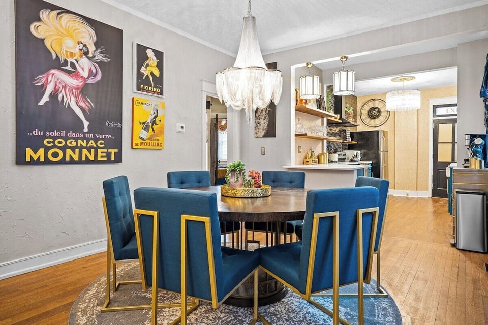 Gather around the lower-level Art Deco dining space featuring plush blue seating, a modern round table, and vintage poster décor—perfect for group meals during your Midtown Kansas City stay.