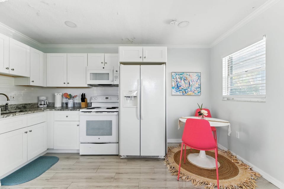 Bright and modern kitchen with crisp white cabinets, granite counters, and full-size appliances. A cozy dining nook with a pop of coral adds charm, making it perfect for enjoying meals after a day of coastal adventures.
