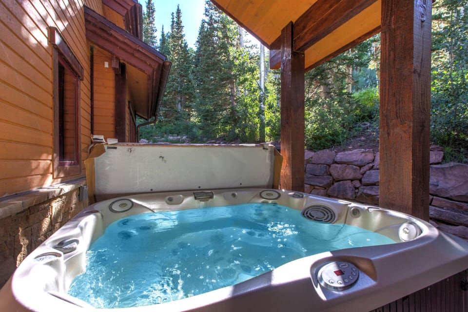 Soak your cares away in your private hot tub, tucked beneath towering pines and framed by rustic stonework—a serene escape where warm bubbles meet mountain air.