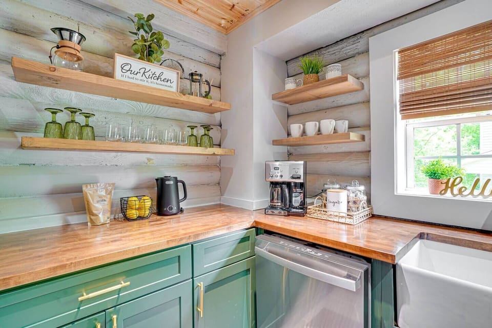 Kitchen with several coffee makers incl. coffee, sugar, creamer & tea, plus dishes, bowls, wine glasses, cook ware & more.
