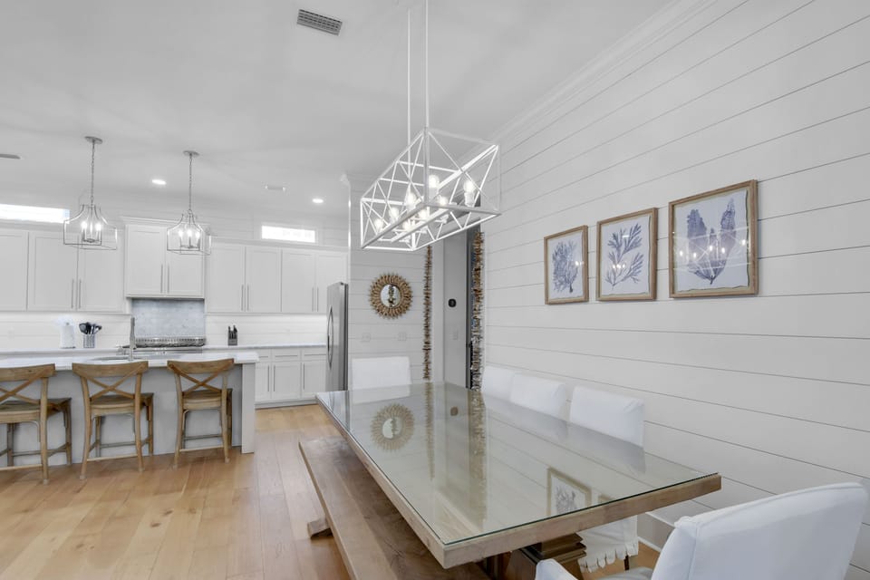 Dining Room at Blue Heron Cottage – Farm Table & Open Kitchen Fl - A long glass farm table seats eight comfortably and flows directly into the kitchen island with three bar stools. Whether it’s pancakes or prosecco, everyone has a seat—and no one’s stuck in the kitchen alone.