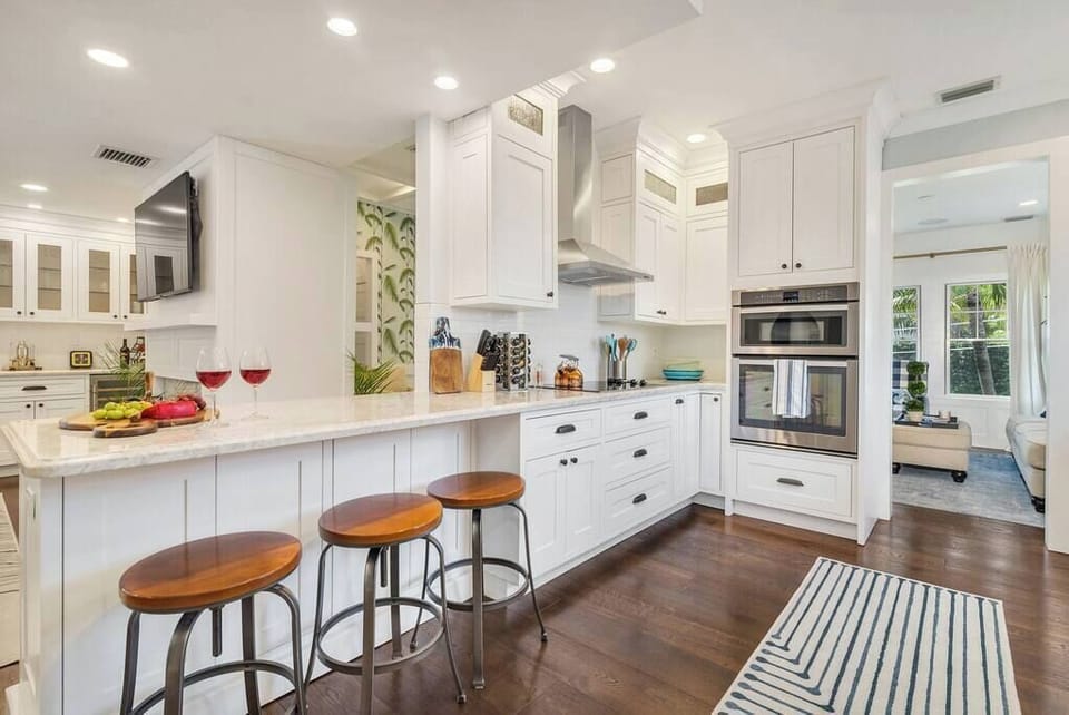 Modern kitchen with white cabinetry, stainless steel appliances, and a breakfast bar with wooden stools.