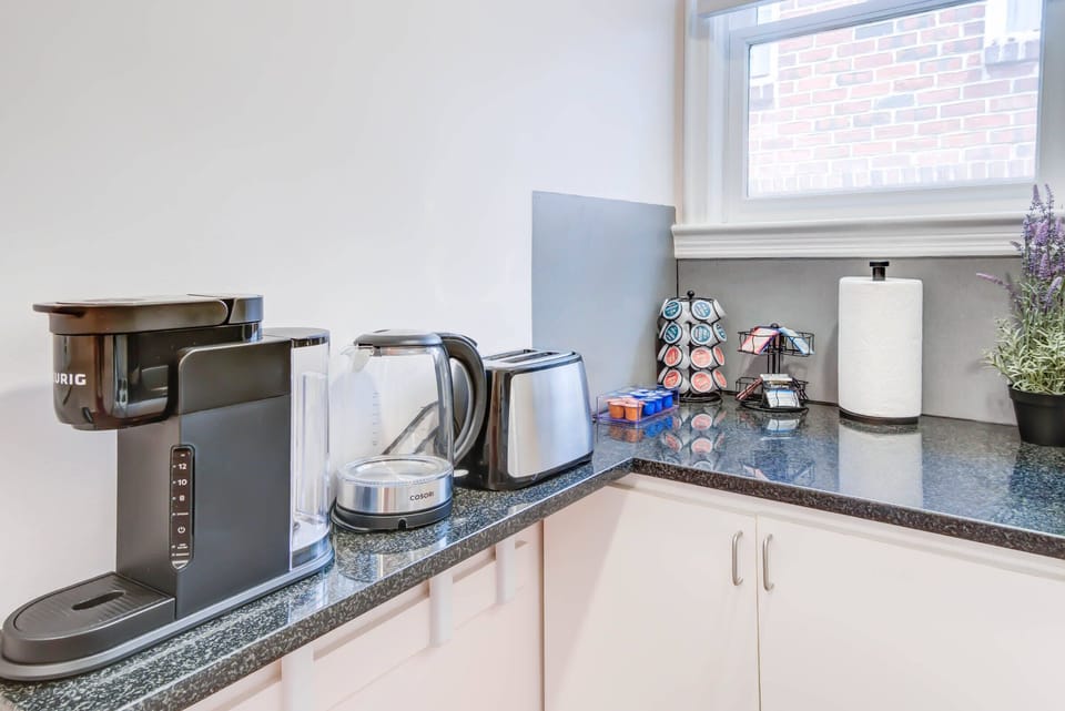 Kickstart your mornings with a complimentary coffee from our fully equipped kitchen, featuring a coffee maker, as natural light floods in through the window.