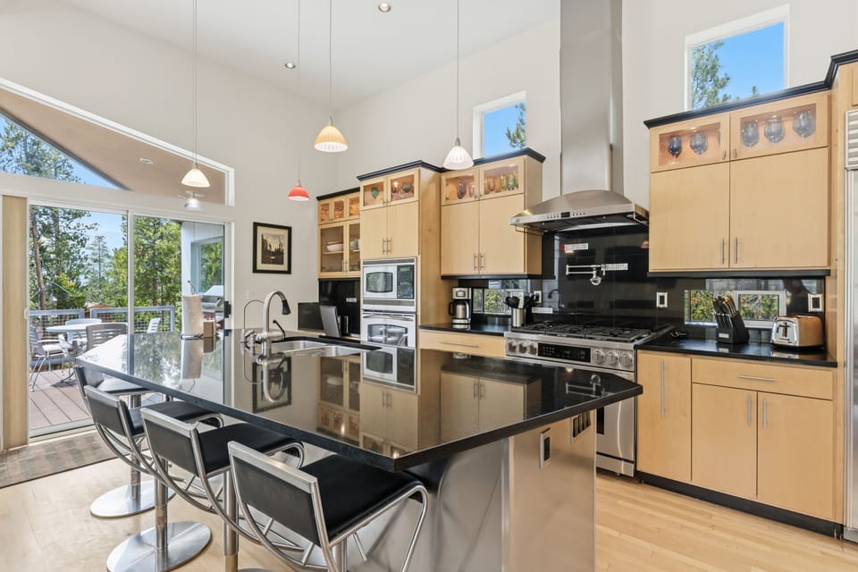 This open, light-filled kitchen and dining space features gleaming black granite countertops, warm wood cabinetry, and stainless appliances—plus a bar seating area and seamless access to your private outdoor deck and natural surroundings.