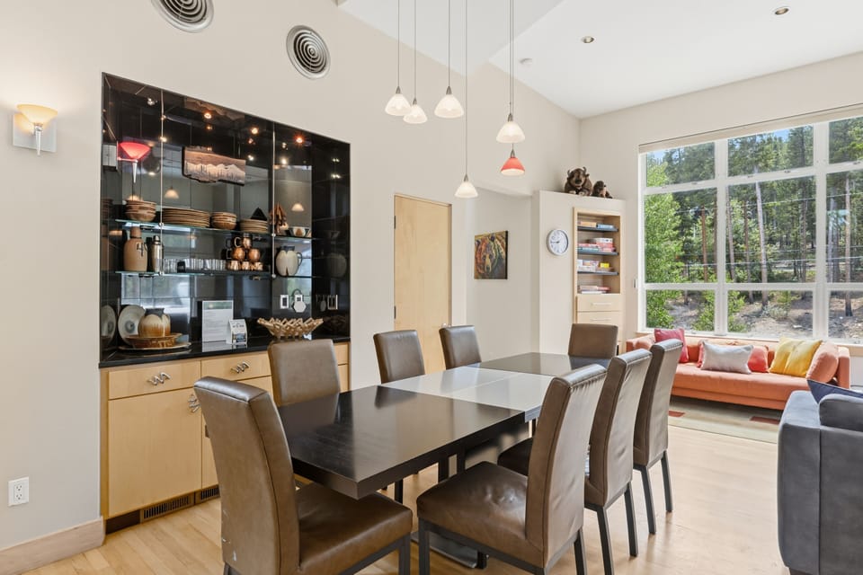 Gather around the elegant dining table where your group can share meals under stylish pendant lighting, with sunlight streaming through floor-to-ceiling windows overlooking the peaceful garden.