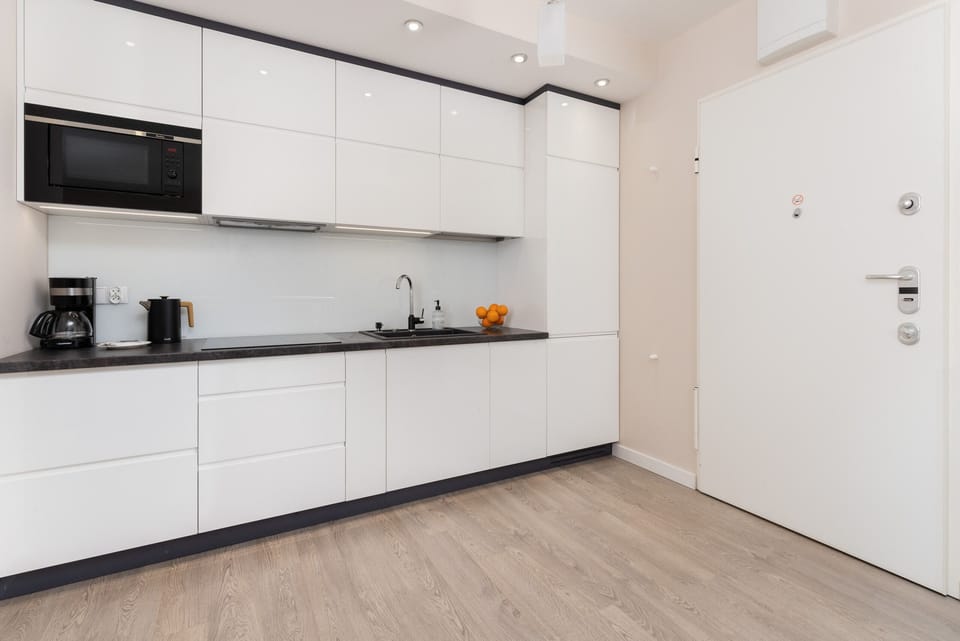 A modern, minimalist kitchen with white cabinetry, black countertops, and plenty of storage space.