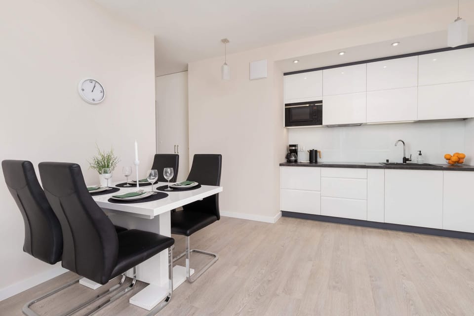 A modern, minimalist kitchen with white cabinetry, black countertops, and plenty of storage space.