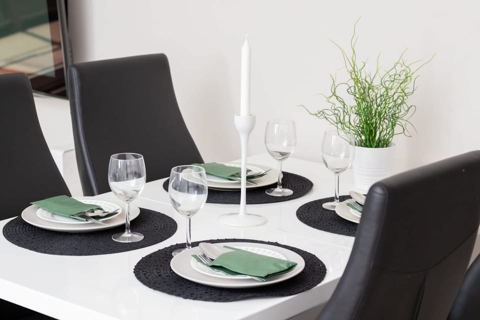 A close-up of a round dining table set elegantly with tableware, glasses, and decorative greenery.