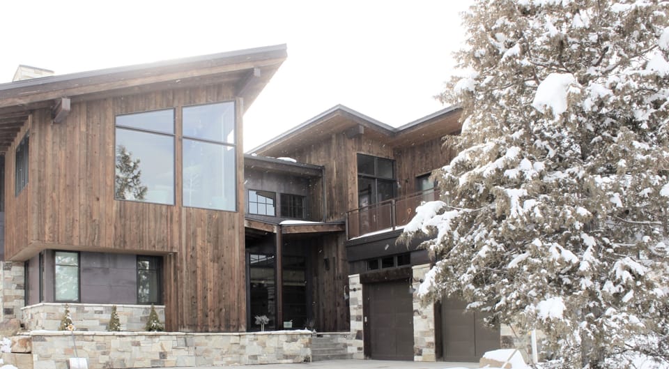 - Rustic mountain home with wood and stone exterior  
- Large windows frame forest and snowy views  
- Spacious modern retreat designed for cozy stays