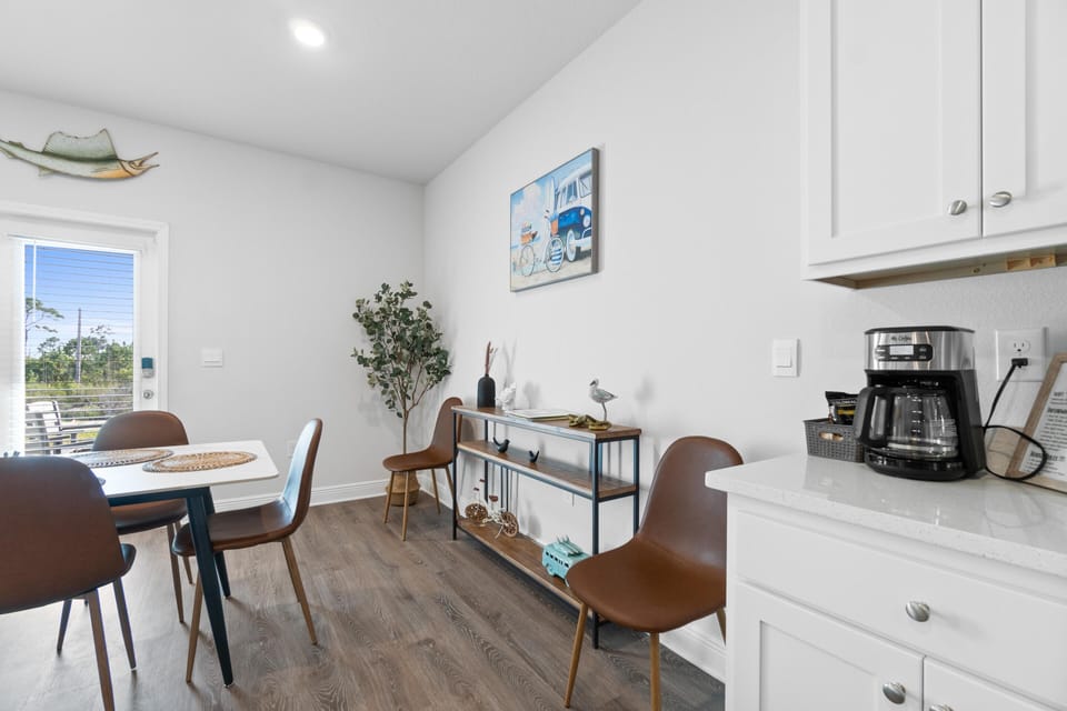 Enjoy morning coffee in your bright, modern kitchen featuring white cabinetry, stylish dining space, and charming coastal artwork that creates a welcoming atmosphere.
