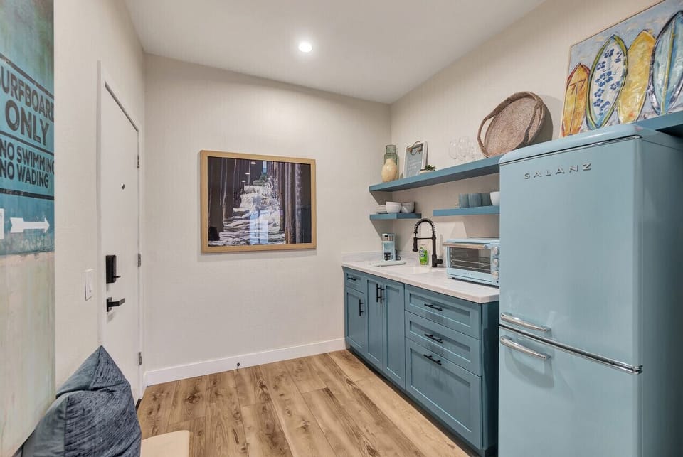 Compact kitchenette w/ sleek counters, open shelving & retro-style fridge
