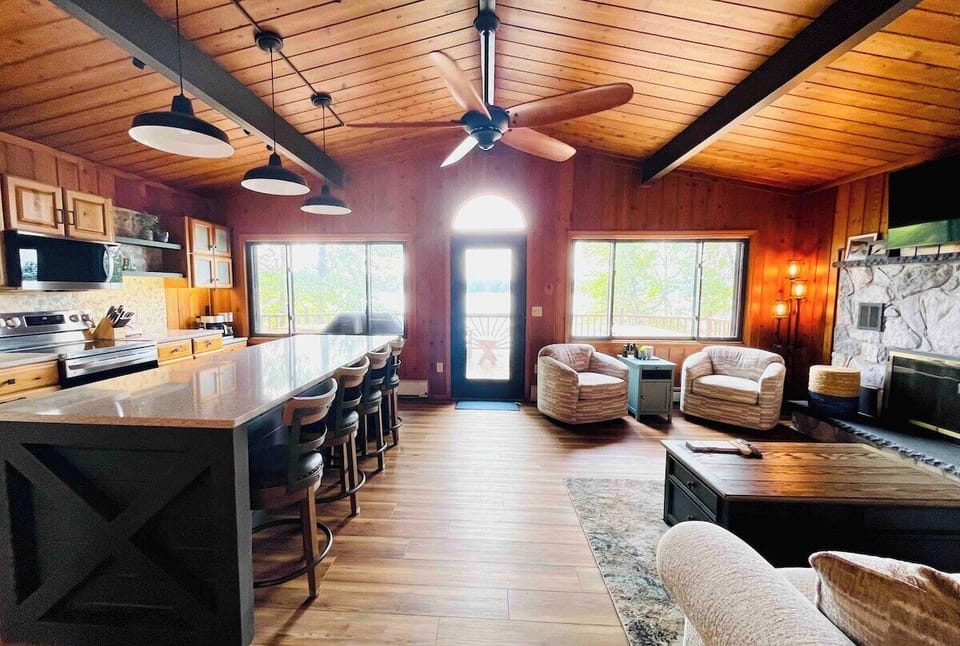 Interior of the kitchen and living room with knotty pine vaulted ceiling and large windows looking out to the lake.