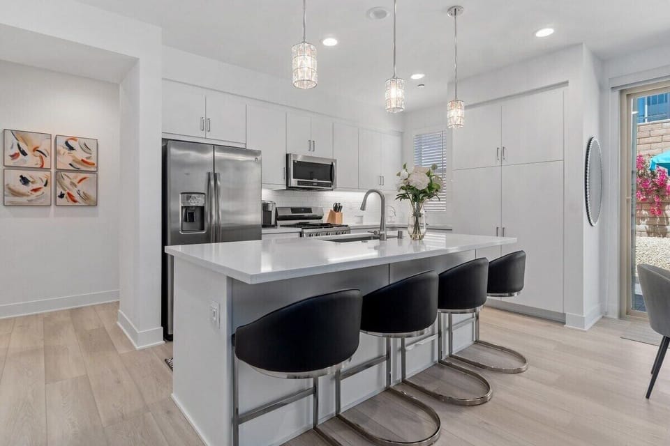 A bright white kitchen with a huge island and bar seating for four at the counter.