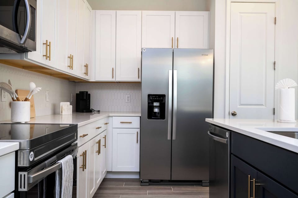 Cook like a pro in our sleek two-tone kitchen boasting white shaker cabinets, navy island, stainless steel appliances, gold hardware & chic hex-tile backsplash-plus plenty of prep space for morning lattes & casual dinners!
