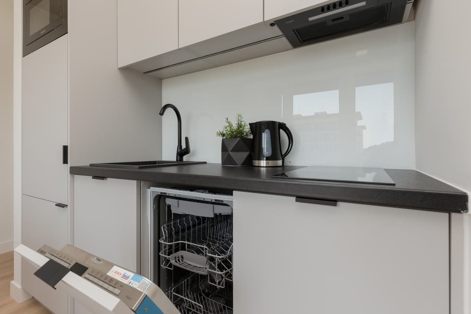 A fully equipped kitchen with clean white cabinetry, a black countertop, and stainless steel appliances.