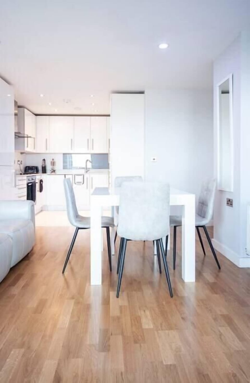 A modern living room on the 12th floor features a 60-inch TV, a dining table with four chairs, and access to a balcony with stunning city views. Two electric reclined sofas provide comfort and a sound system offer entertainment.