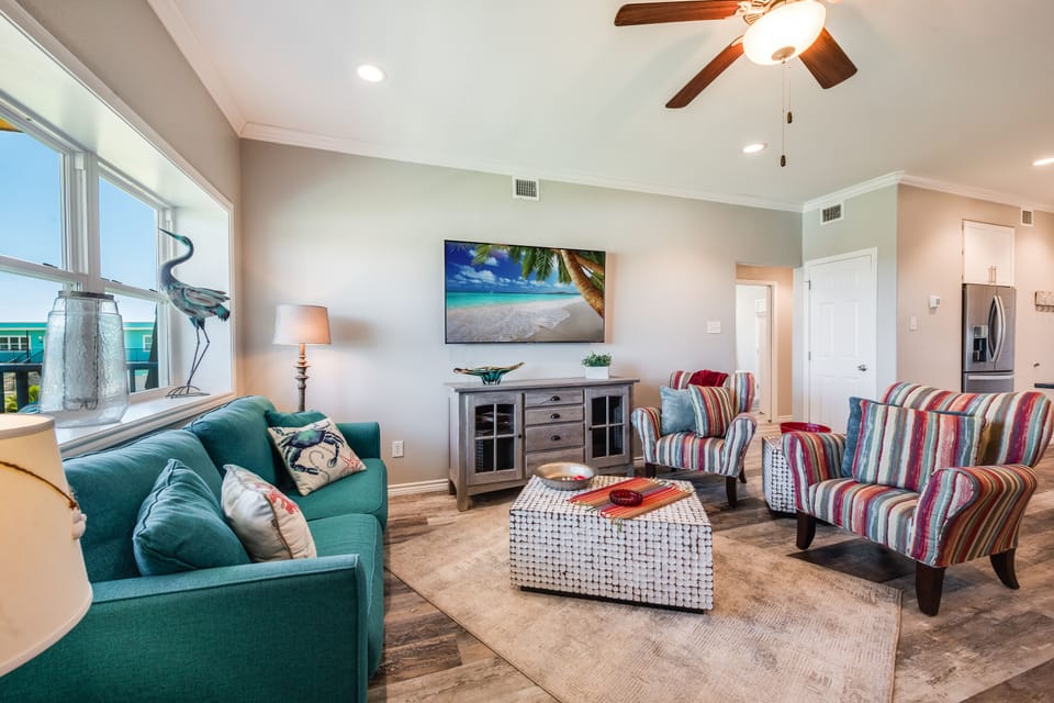 Unwind in your bright living room featuring a cozy teal sofa, colorful striped chairs, and tropical artwork—perfect for relaxing after beachside adventures.
