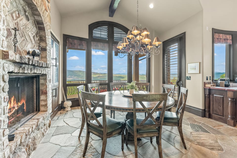 - Dining room with round table and chandelier lighting  
- Large windows overlooking mountains and balcony seating  
- Stone fireplace adds warmth to family meals