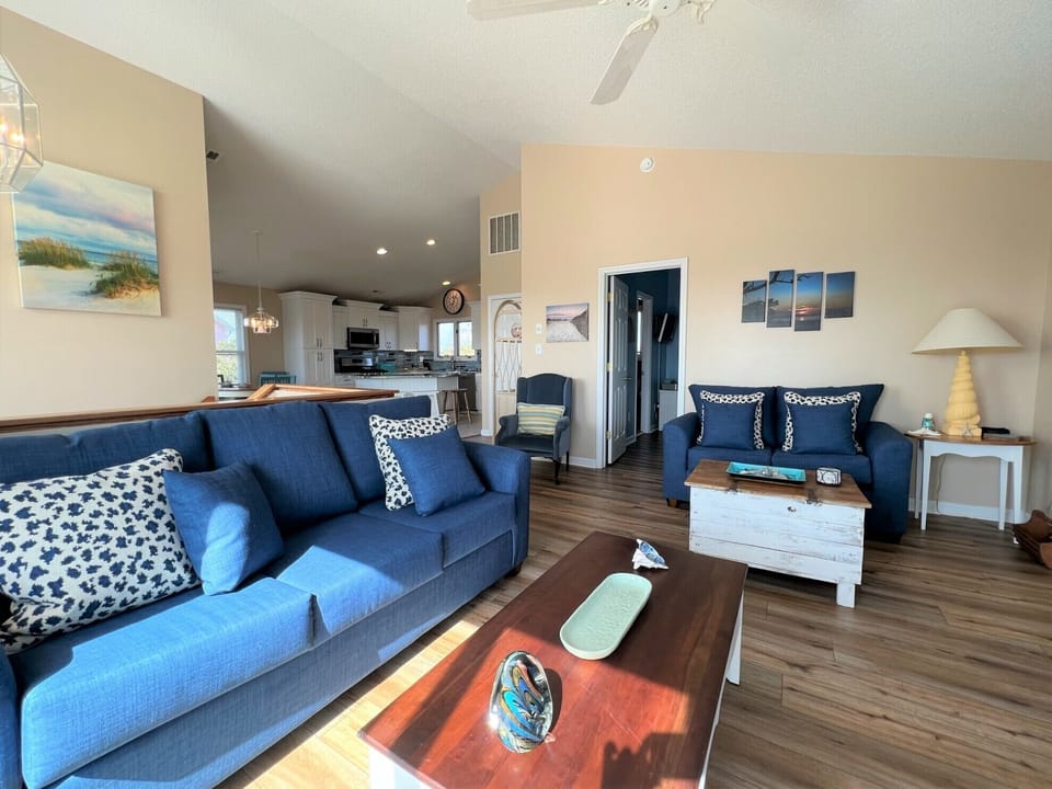 Sink into plush navy sofas in your bright, airy living space where coastal artwork and warm lighting create the perfect atmosphere for relaxation.