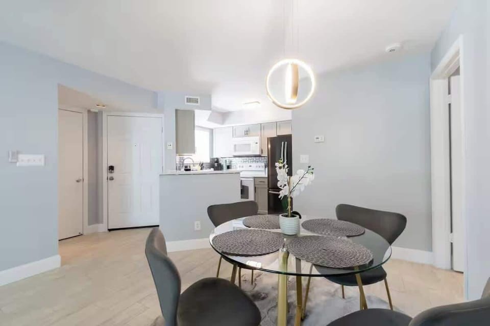 Dining area with a round table and four chairs, open to the kitchen, with light wood floors and a pendant light overhead.
