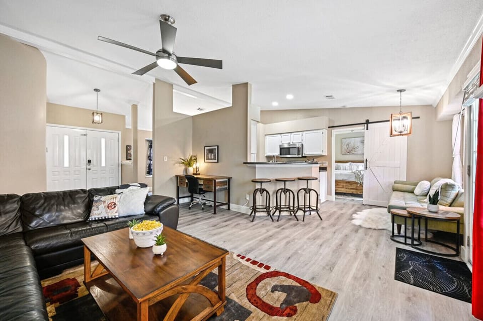 Open‑concept living room at Saloma Place with leather sectional, dedicated workspace, breakfast bar, and bright kitchen—perfect Austin home base for groups.