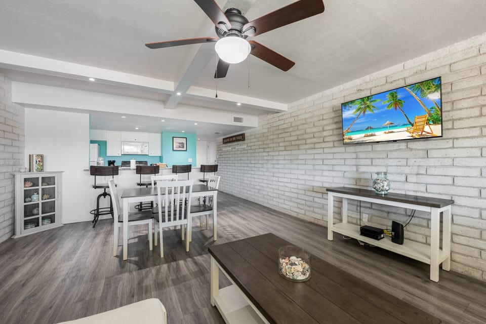 Relax in your bright, open-concept living space featuring exposed brick walls, modern furnishings, and a large TV for cozy movie nights together.