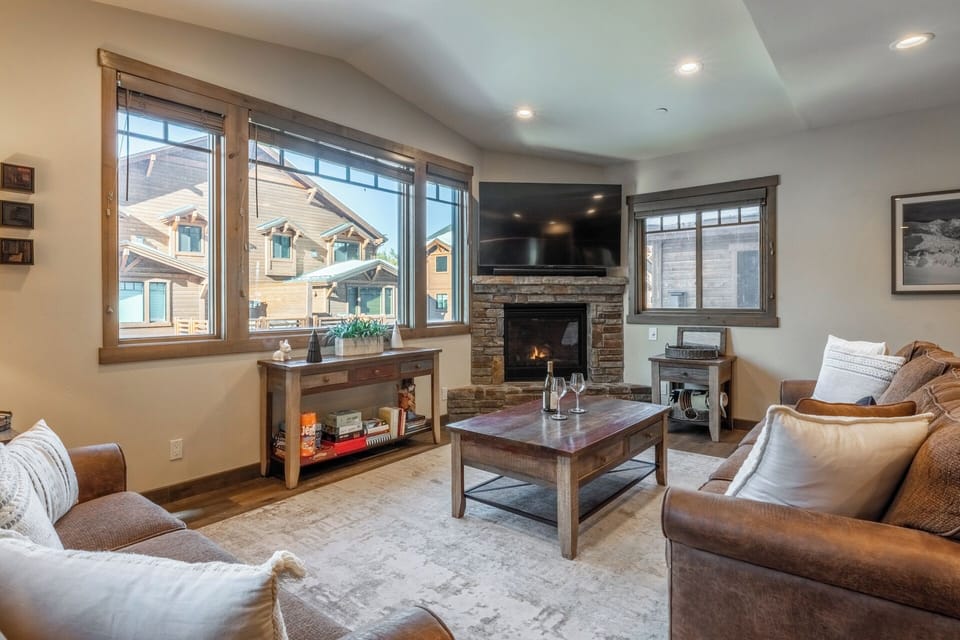 Mountain light pours through expansive windows, framing a warm fireside living space with oversized seating and room for everyone to gather.