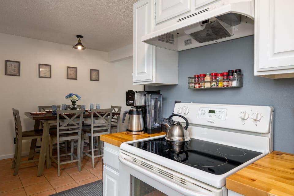 Butcherblock style countertops on either side of an induction stove/oven combo. Coffee maker to the left and knife block to the right.