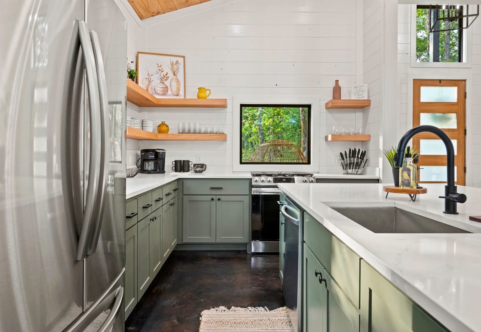 This streamlined kitchen features a mix of natural wood shelves and modern green cabinetry, providing a bright and functional space for culinary creativity.