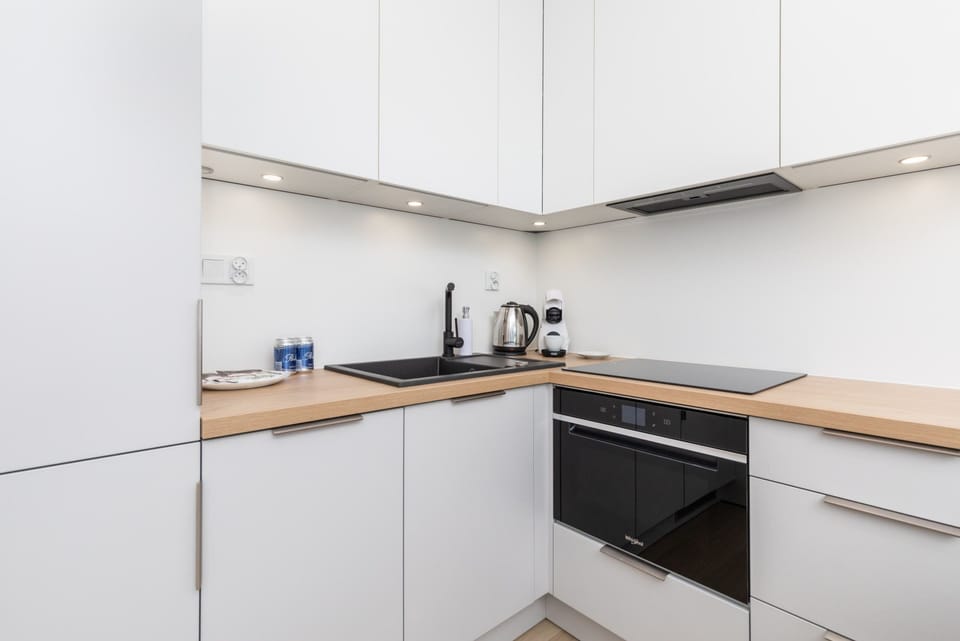 A modern kitchenette with sleek white cabinetry, a black stovetop, and wooden countertops for a minimalist and functional design.
