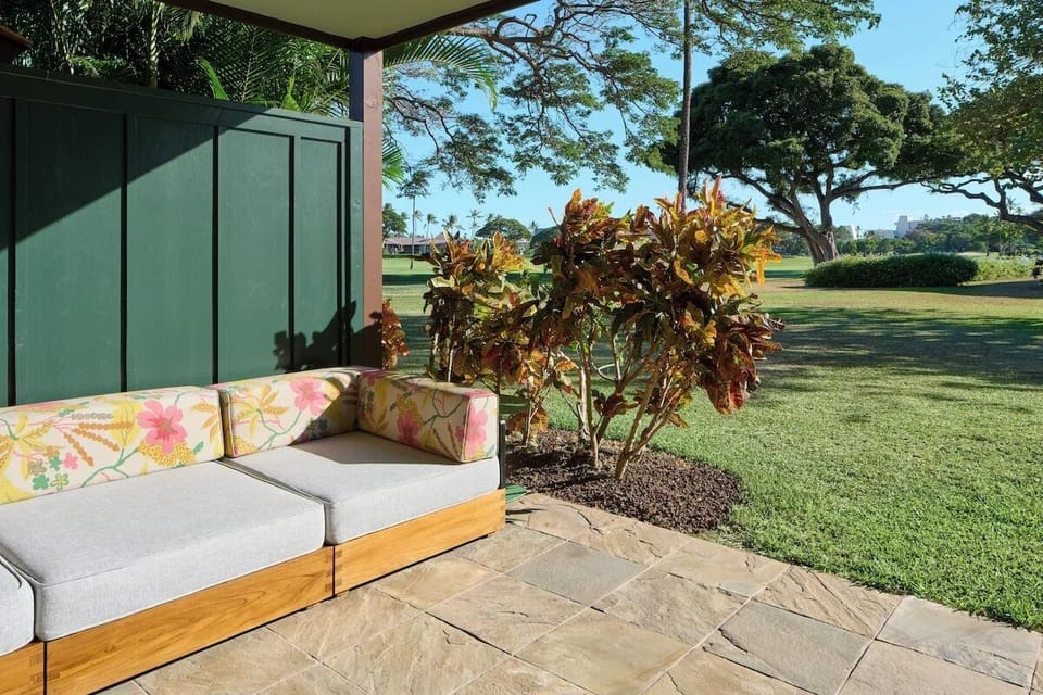 Lounge outdoors on cushioned seating beside lush tropical grounds.