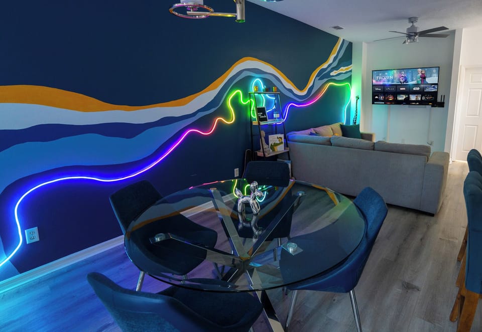 Open concept living and dining area with neon wall art and painted colorful wave