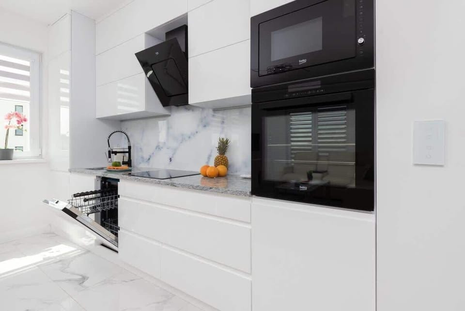 A modern kitchen with sleek white cabinetry, black appliances, and marble-style backsplash for a luxurious look.
