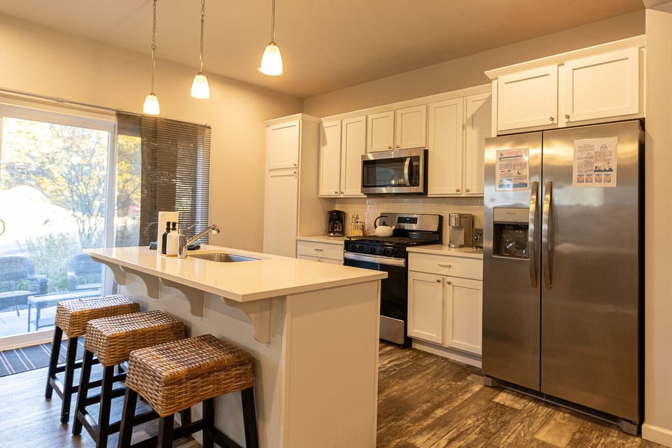 This spacious, modern kitchen at Harbor Pointe features stainless steel appliances, a large island with seating, and plenty of counter space for cooking and gathering. Sliding doors open to the outdoor patio creating an easy indoor-outdoor flow for meals and entertaining.