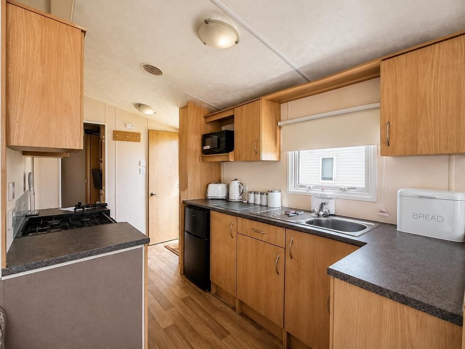 Natural light brightens the kitchen with wood cabinets, black appliances, and a stainless steel sink beneath the window.