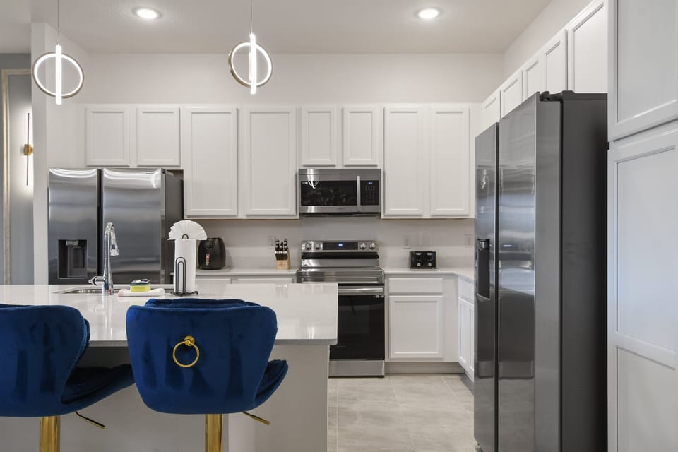 Modern chef’s kitchen with sleek appliances, bright cabinetry, and stylish seating