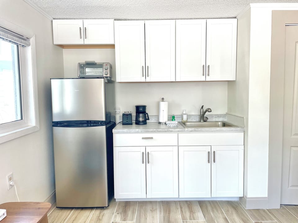 Compact kitchenette with white cabinetry, stainless refrigerator, and coffee maker
