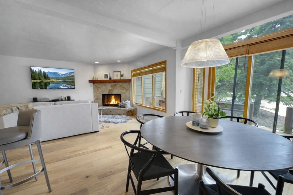 Gather around the sleek dining table while your crackling fireplace sets a cozy mood and natural light streams through windows.