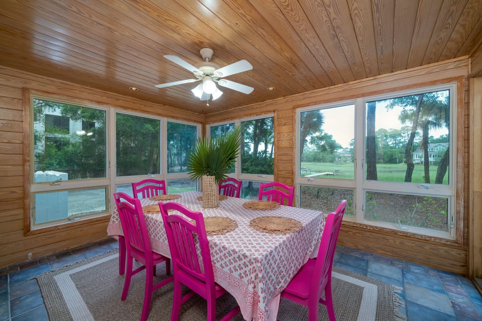 The room has floor to ceiling windows on three walls. A dining table can seat 8