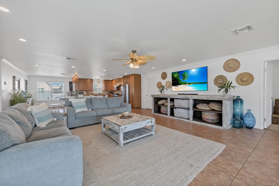 Sink into plush coastal comfort in this bright open-concept living space featuring ocean-blue sofas and tropical decor touches.