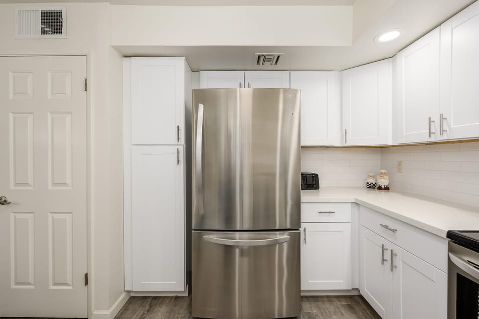 Stainless steel refrigerator centers white shaker cabinets and quartz countertops with subway tile backsplash in the kitchen.