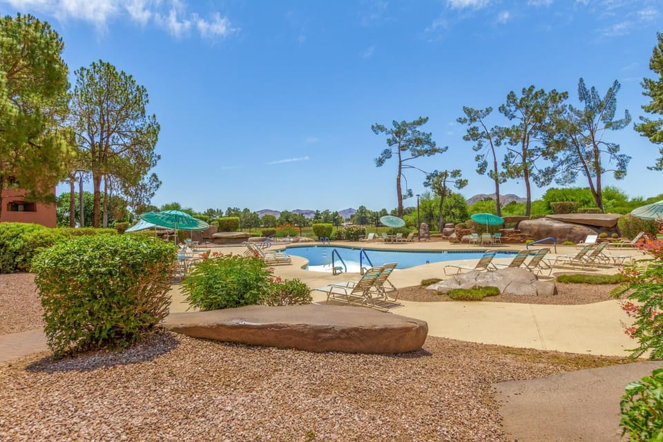 Heated pool surrounded by concrete deck, lounge chairs, teal umbrellas, desert landscaping, and distant mountain views.
