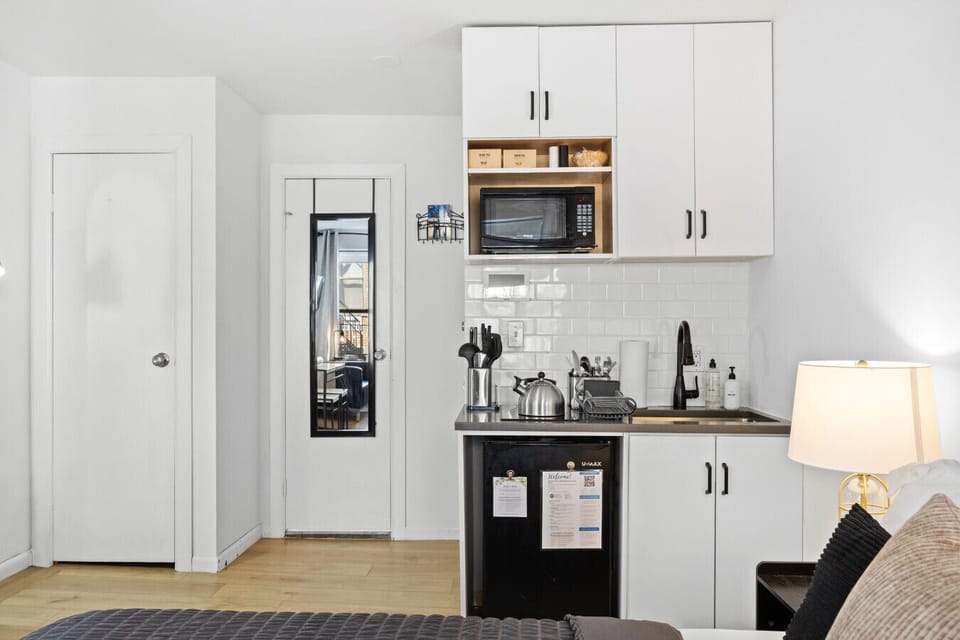 Kitchen with white cabinets, counter, microwave, sink, and black fridge. Tea box on shelf, mirror on nearby door.